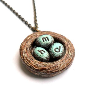May include: A brown ceramic bird's nest necklace with three turquoise blue eggs that have the letters 'h', 'm', and 'd' on them.