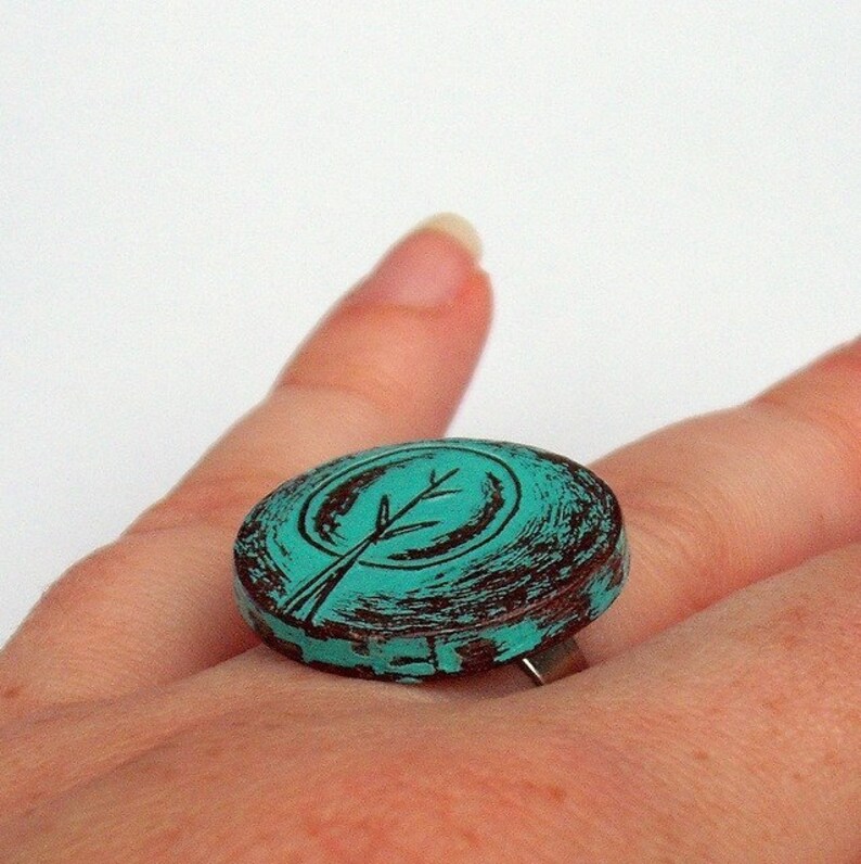 May include: Teal blue ring with a brown distressed finish. The ring features a stylized tree design.