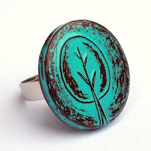 May include: A turquoise and brown ring with a stylized tree design. The ring is made of metal and has a distressed finish.