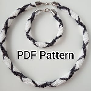 Könnte beinhalten: Ein schwarzes und weißes Perlen-Halsketten- und Armband-Set mit einem Diamantenmuster. Das Set enthält einen Verschluss. Das Bild enthält den Text "PDF Pattern".