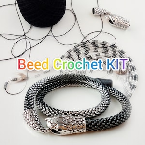 Puede incluir: Un kit de crochet de cuentas con cuentas negras y plateadas, hilo negro y dos cierres de cabeza de serpiente plateados. El kit incluye el texto "Bead Crochet KIT".