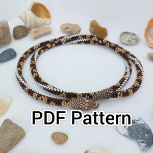 Könnte beinhalten: Eine Perlenkette mit einem schlangenförmigen Verschluss. Die Halskette hat ein Muster aus braunen, weißen und beigen Perlen. Das Bild enthält den Text "PDF Pattern". Muscheln und Steine befinden sich im Hintergrund.