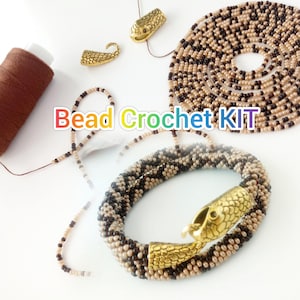Könnte beinhalten: Ein Perlen-Häkel-Set mit Schlangenmotiv. Das Set enthält ein teilweise fertiges Armband mit einem goldfarbenen Schlangenkopfverschluss, Perlen in Braun- und Schwarztönen und eine braune Garnrolle. Der Text "Bead Crochet KIT" ist ebenfalls sichtbar.