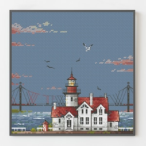 Könnte beinhalten: Kreuzstich-Kunst einer Küstenlandschaft mit einem weißen Leuchtturm, rotem Dach und einer Brücke im Hintergrund. Der Himmel ist blau mit Wolken und Vögeln. Das Kunstwerk ist in einem grauen Rahmen gerahmt.
