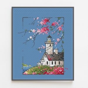 May include: A cross-stitch pattern of a white lighthouse with a black roof and a red door, surrounded by pink flowers and a blue sky.