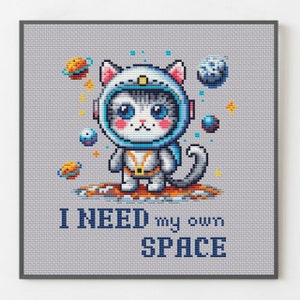 Könnte beinhalten: Ein Kreuzstichmuster mit einer Cartoon-Katze, die einen Astronautenhelm und einen Raumanzug trägt. Die Katze steht auf einem Planeten mit Sternen und anderen Planeten im Hintergrund. Der Text "I NEED my own SPACE" befindet sich unter der Katze.