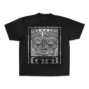 May include: Black t-shirt featuring a detailed, grayscale graphic of a stylized face within a rectangular frame. The design includes intricate patterns and the word "TOOL" at the bottom. The shirt is a classic crew neck style.
