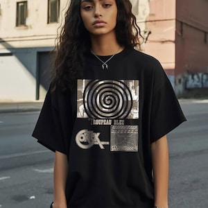 May include: Black t-shirt with a graphic print featuring a spiral design, the text "Troupeu Bleu", and a geometric pattern.