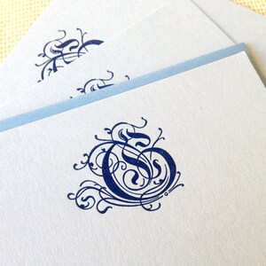 May include: A white card with a blue border and a navy blue calligraphic letter G monogram.