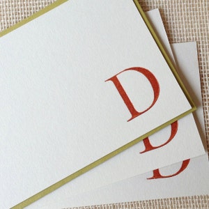 May include: Three white note cards with a green border. The top card has a large, red letter "D" printed on it. The other two cards have smaller, red letters "D" printed on them.