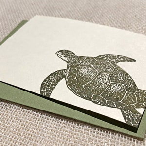 May include: A green and white greeting card with a detailed illustration of a sea turtle swimming.