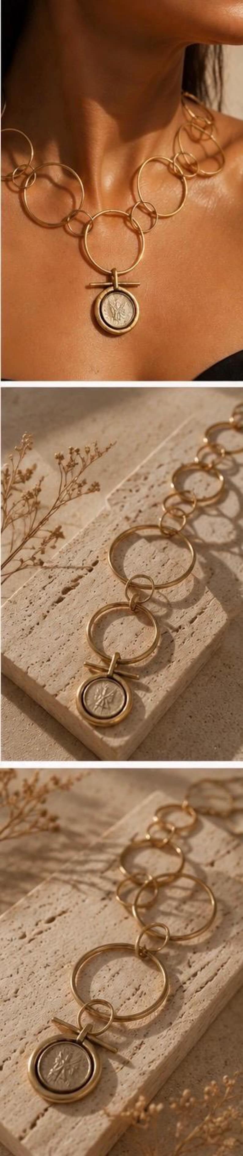 May include: A gold-toned necklace featuring a series of interlocking circular links of varying sizes. The necklace includes a central pendant consisting of a circular coin-like charm suspended from a horizontal bar attached to a larger ring.
