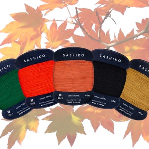 May include: Five spools of Sashiko thread in different colours: green, orange, brown, black, and gold. Each spool is labelled "Sashiko" and has the text "cotton 100%", "20/4", "daruma-ito.co.jp", and "MADE IN JAPAN".