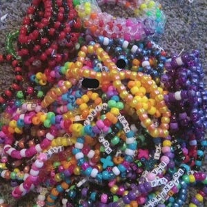 Può includere: Un grande mucchio di braccialetti colorati con perline, alcuni con perline a lettere che compongono parole come "BREAKIN" e "TOH".