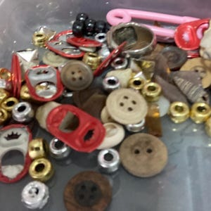 May include: A collection of assorted buttons, beads, and other trinkets in a clear plastic container. The items are mostly red, gold, and brown.