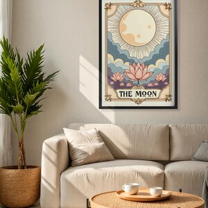 May include: A vintage-style tarot card illustration of The Moon card. The card features a full moon with rays of light, clouds, and three pink lotus flowers. The text "THE MOON" is printed in a decorative font at the bottom of the card.