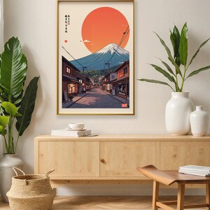 Pode incluir: Uma impress&atilde;o emoldurada de uma cena de rua japonesa com o Monte Fuji ao fundo. O sol se p&otilde;e atr&aacute;s da montanha, lan&ccedil;ando um brilho quente sobre a cena. A rua &eacute; ladeada por edif&iacute;cios tradicionais japoneses, e h&aacute; pessoas caminhando pela rua.