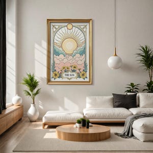 May include: A gold framed print of a tarot card depicting a sun with rays and clouds in a pastel color scheme. The card is titled "THE SUN".