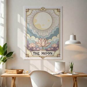 May include: A vintage-style tarot card illustration featuring a full moon with rays of light, surrounded by clouds and pink lotus flowers. The card is titled "THE MOON".
