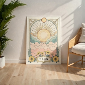 May include: A vintage-style tarot card print featuring the Sun card. The card depicts a sun with rays, clouds, and flowers in a yellow, pink, and blue color scheme. The text "THE SUN" is printed at the bottom of the card.