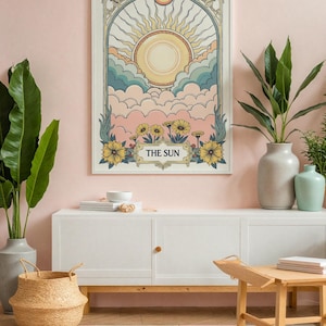 May include: A white framed print with a vintage illustration of a sun with rays and clouds. The print has the words "THE SUN" at the bottom. The print is hanging on a pink wall above a white cabinet with a wooden top.