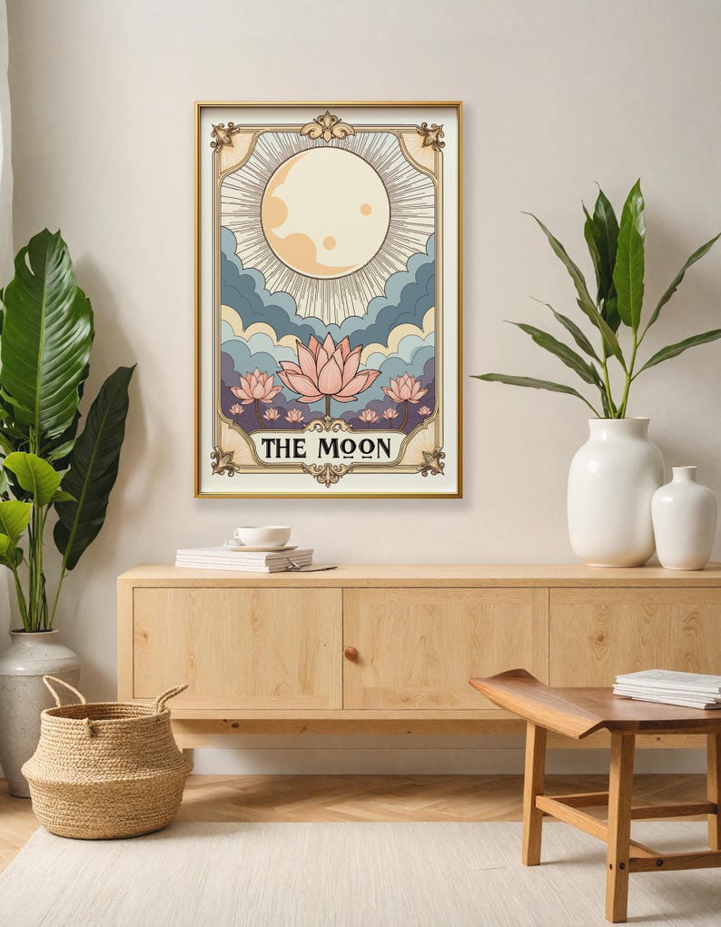 May include: A vintage-style tarot card illustration of The Moon card. The card features a full moon with rays of light, clouds, and pink lotus flowers. The text "THE MOON" is printed in black at the bottom of the card.