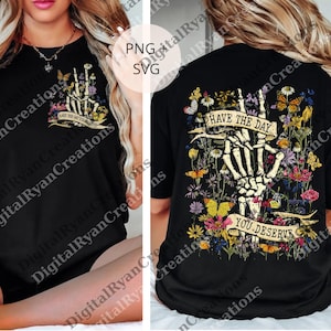 Peut inclure: T-shirt noir avec un motif de main de squelette entourée de fleurs et de papillons. Le devant du t-shirt porte l'inscription "HAVE THE DAY YOU DESERVE". Le dos du t-shirt porte l'inscription "HAVE THE DAY" et "YOU DESERVE".
