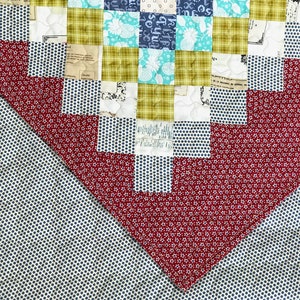 May include: Close-up of a patchwork quilt with a variety of patterned fabrics. The quilt features squares of teal, navy, and olive green fabrics, along with red and white polka dot and floral patterns. The quilt is a mix of textures and colors.