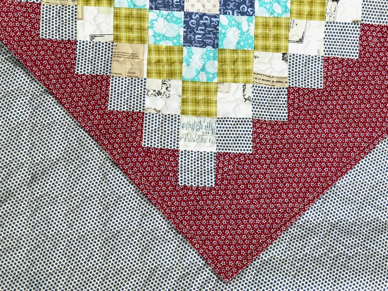May include: Close-up of a patchwork quilt with a variety of patterned fabrics. The quilt features squares of teal, navy, and olive green fabrics, along with red and white polka dot and floral patterns. The quilt is a mix of textures and colors.