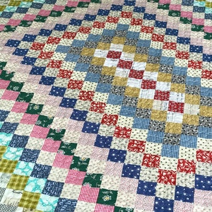 May include: A handmade quilt with a patchwork design. The quilt features a variety of fabrics in a square pattern, with colors including red, blue, green, pink, and white. The quilt has a diamond-shaped center.