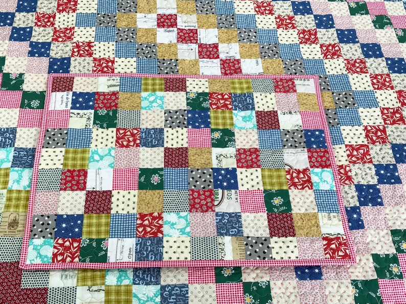 May include: A patchwork quilt and placemat set. The quilt features a grid pattern of various fabric squares in red, blue, green, white, and tan. The placemat has a red gingham border and matches the quilt's color scheme.