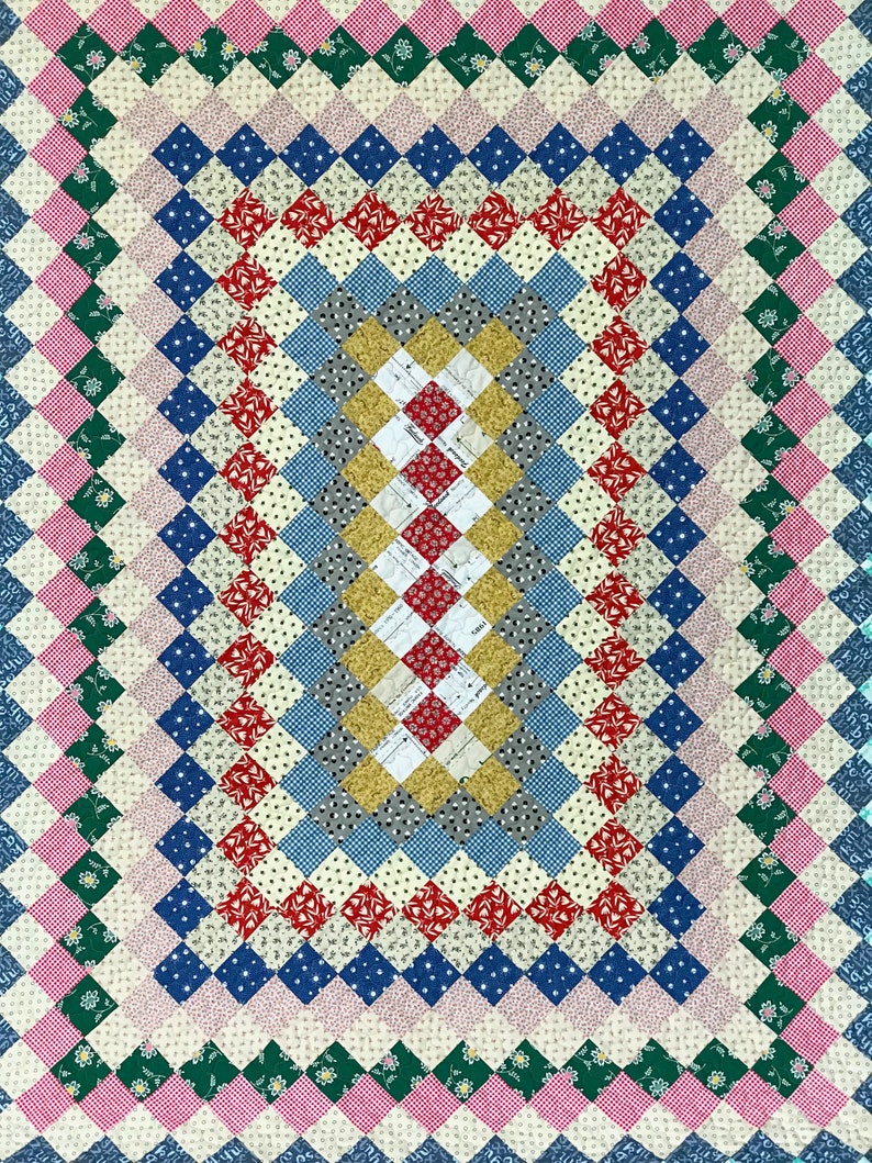 May include: A colorful quilt with a diamond pattern. The quilt features a variety of fabrics in shades of pink, green, blue, red, and yellow. The design is symmetrical, with a central rectangular pattern surrounded by borders.