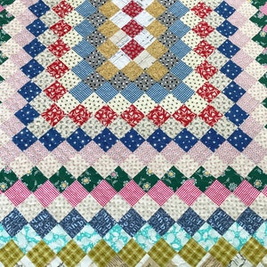 May include: A handmade quilt with a diamond pattern in various colors. The quilt features red, blue, white, green, and yellow squares. The design includes floral, polka dot, and plaid patterns, creating a patchwork effect. The quilt is a cozy, decorative textile.