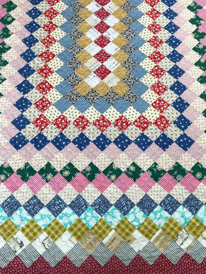 May include: A handmade quilt with a diamond pattern in various colors. The quilt features red, blue, white, green, and yellow squares. The design includes floral, polka dot, and plaid patterns, creating a patchwork effect. The quilt is a cozy, decorative textile.