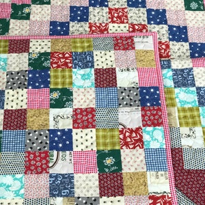 May include: A patchwork quilt with a variety of patterned squares in red, pink, green, blue, and tan. The quilt has a red and white gingham border. The squares feature floral, polka dot, and geometric designs.
