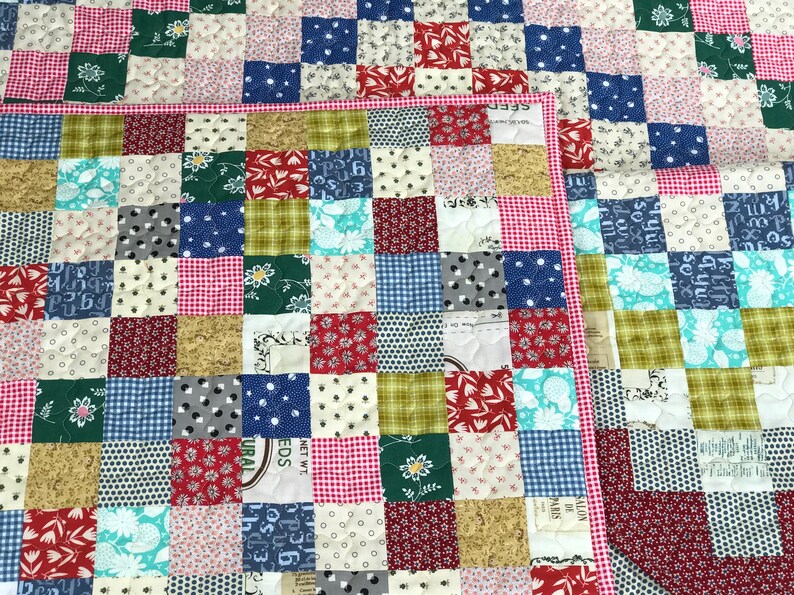 May include: A patchwork quilt with a variety of patterned squares in red, pink, green, blue, and tan. The quilt has a red and white gingham border. The squares feature floral, polka dot, and geometric designs.