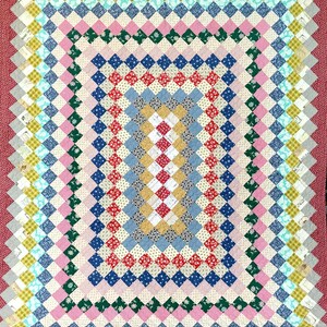 May include: A colorful patchwork quilt with a repeating diamond pattern in various colors including red, blue, pink, green, and yellow. The quilt has a scalloped edge and a solid red border. The quilt is approximately 60 inches by 70 inches.