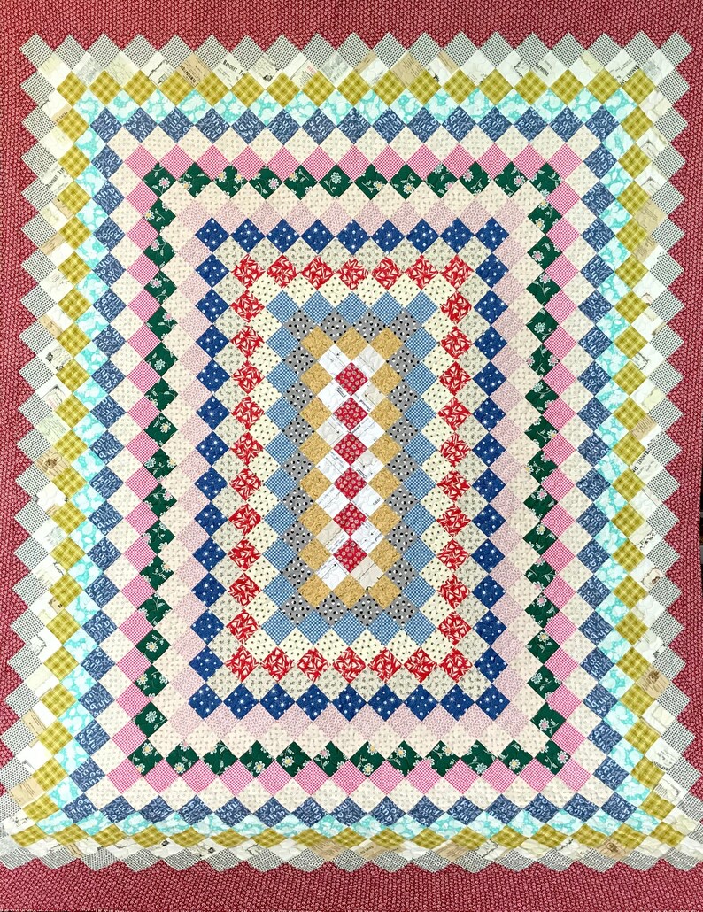 May include: A colorful patchwork quilt with a repeating diamond pattern in various colors including red, blue, pink, green, and yellow. The quilt has a scalloped edge and a solid red border. The quilt is approximately 60 inches by 70 inches.