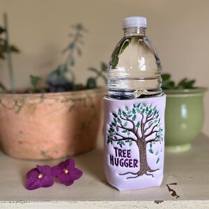 Puede incluir: Un porta botellas de color morado con un árbol verde bordado y el texto "Tree Hugger".