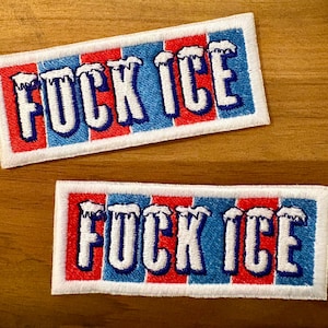 May include: Two rectangular embroidered patches with the words "FUCK ICE" in white, outlined in blue and red. The patches have a white border and are set against a wooden background. The text is stylized with a dripping ice effect.