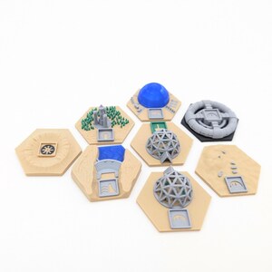 Könnte beinhalten: Eine Sammlung beigefarbener sechseckiger Spielsteine mit verschiedenen 3D-gedruckten Strukturen. Zu den Strukturen gehören eine blaue Kuppel, eine graue geodätische Kugel, ein grauer Ring und ein Miniaturwald. Einige Steine haben kleine graue Anzeigen.
