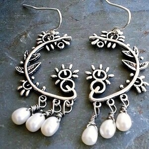 May include: Silver hoop earrings with a floral design and dangling pearl drops.