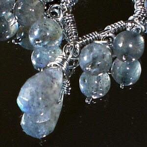 May include: A silver wire wrapped necklace with a cluster of iridescent blue-grey gemstone beads. The beads are of varying sizes and shapes, and some have a pearlescent sheen.