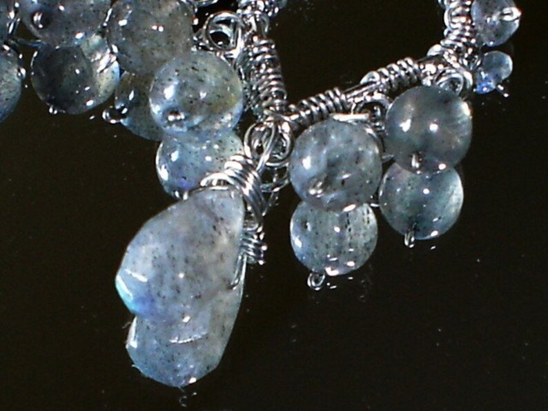 May include: A silver wire wrapped necklace with a cluster of iridescent blue-grey gemstone beads. The beads are of varying sizes and shapes, and some have a pearlescent sheen.
