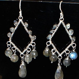 May include: Silver dangle earrings with a diamond-shaped frame and multiple teardrop-shaped iridescent blue-grey stones.