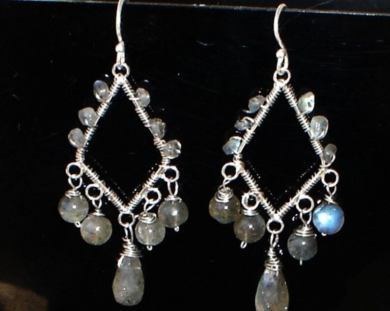 May include: Silver dangle earrings with a diamond-shaped frame and multiple teardrop-shaped iridescent blue-grey stones.