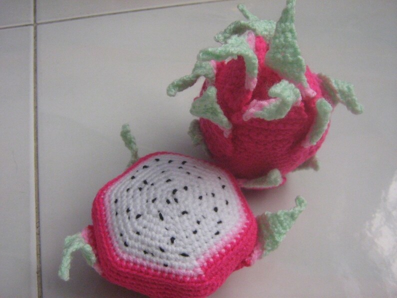 May include: Two crocheted dragon fruit toys. One is pink with green leaves and the other is pink and white with a white center and black seeds.