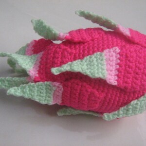 May include: A crocheted pink and green dragon fruit plush toy. The fruit is pink with green accents and has a textured surface.