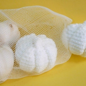 May include: Four white onions in a white mesh bag. The onions are arranged in a circle with one onion on top of the others. The bag is on a yellow surface.