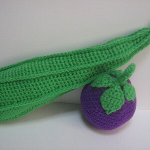 May include: A crocheted green bean with a purple aubergine. The bean is long and thin, while the aubergine is round and has a green stem.